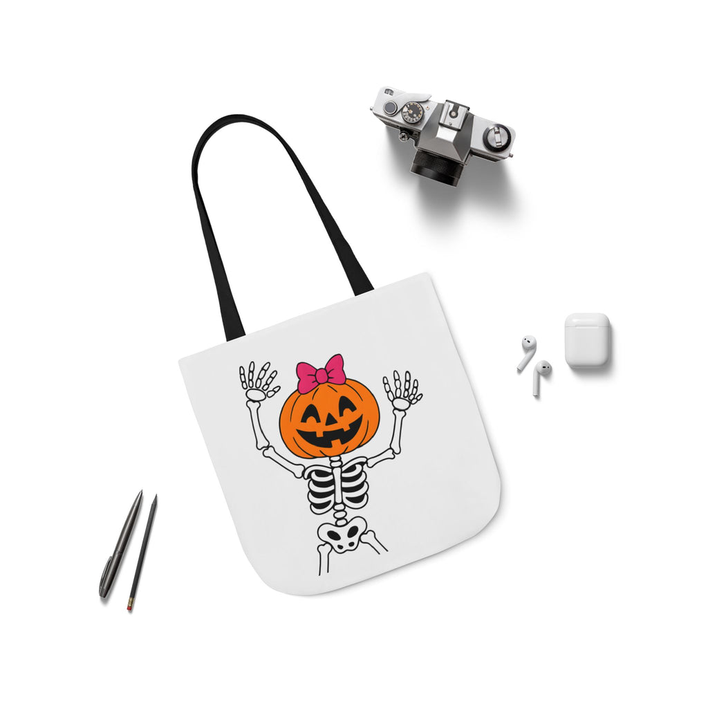 White canvas tote bag with black handles and pumpkin skeleton print, angled flat lay