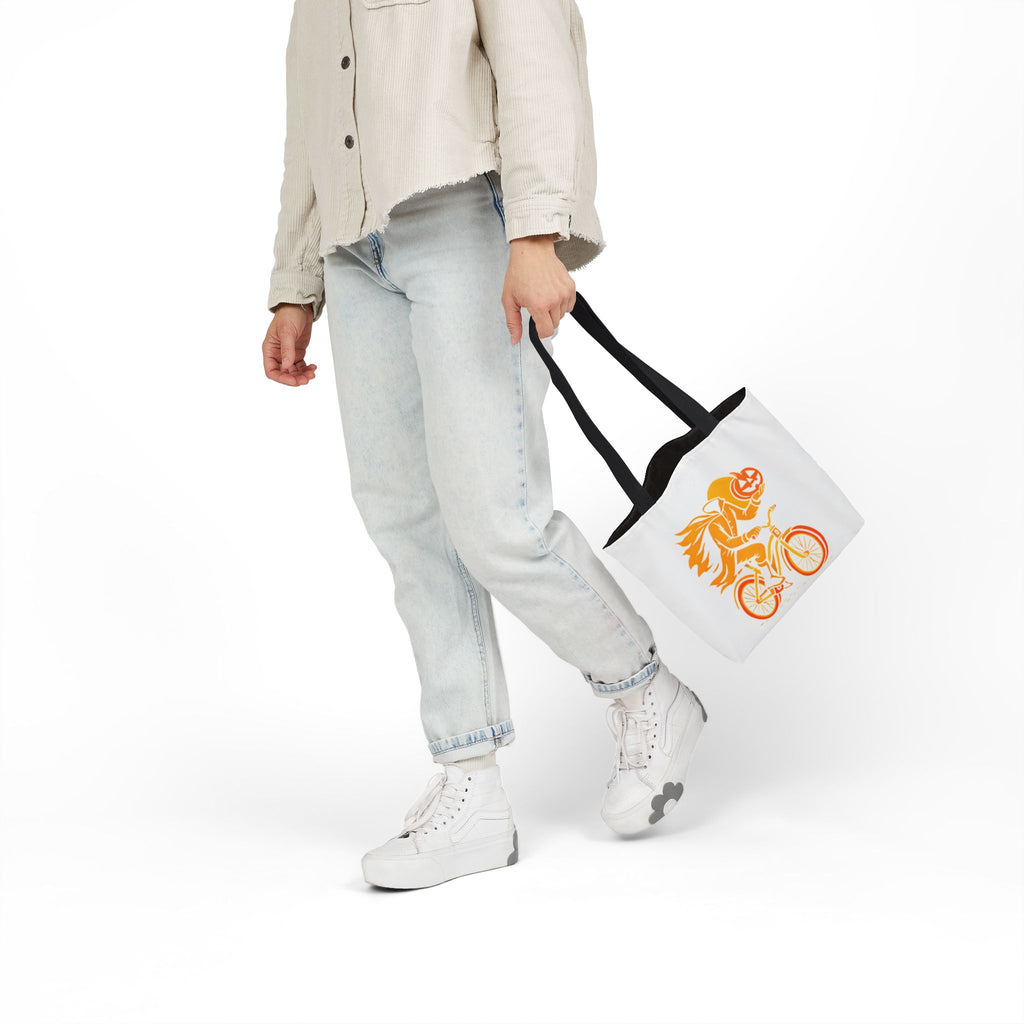 White canvas tote bag with black handles, orange ghost rider pumpkin head on bicycle