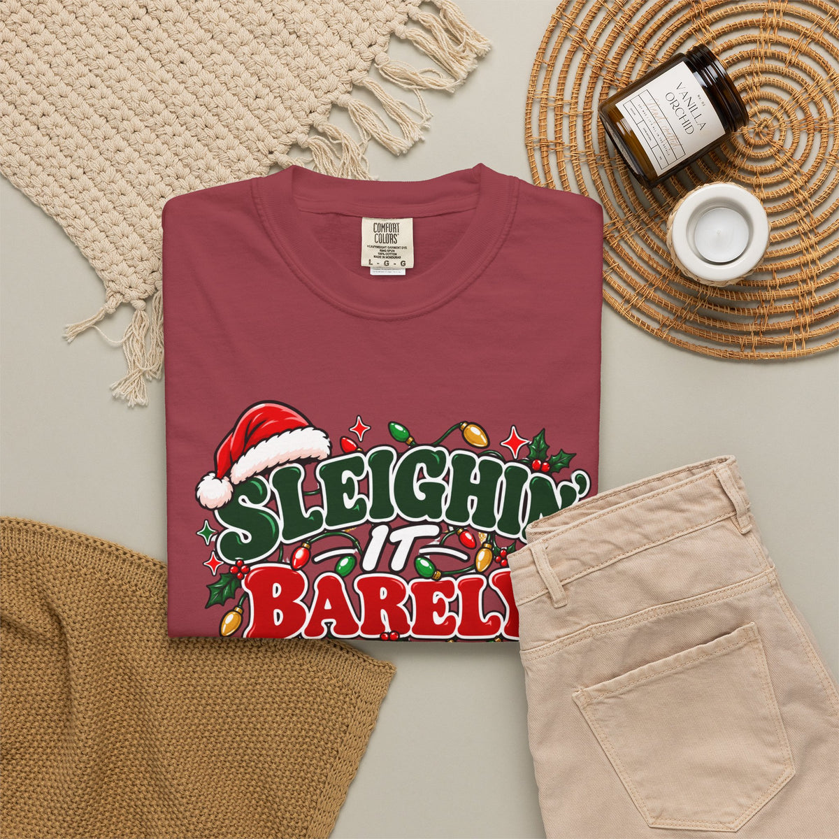 Burgundy crewneck t-shirt with "Sleighin' It Barely" holiday graphic, flat lay