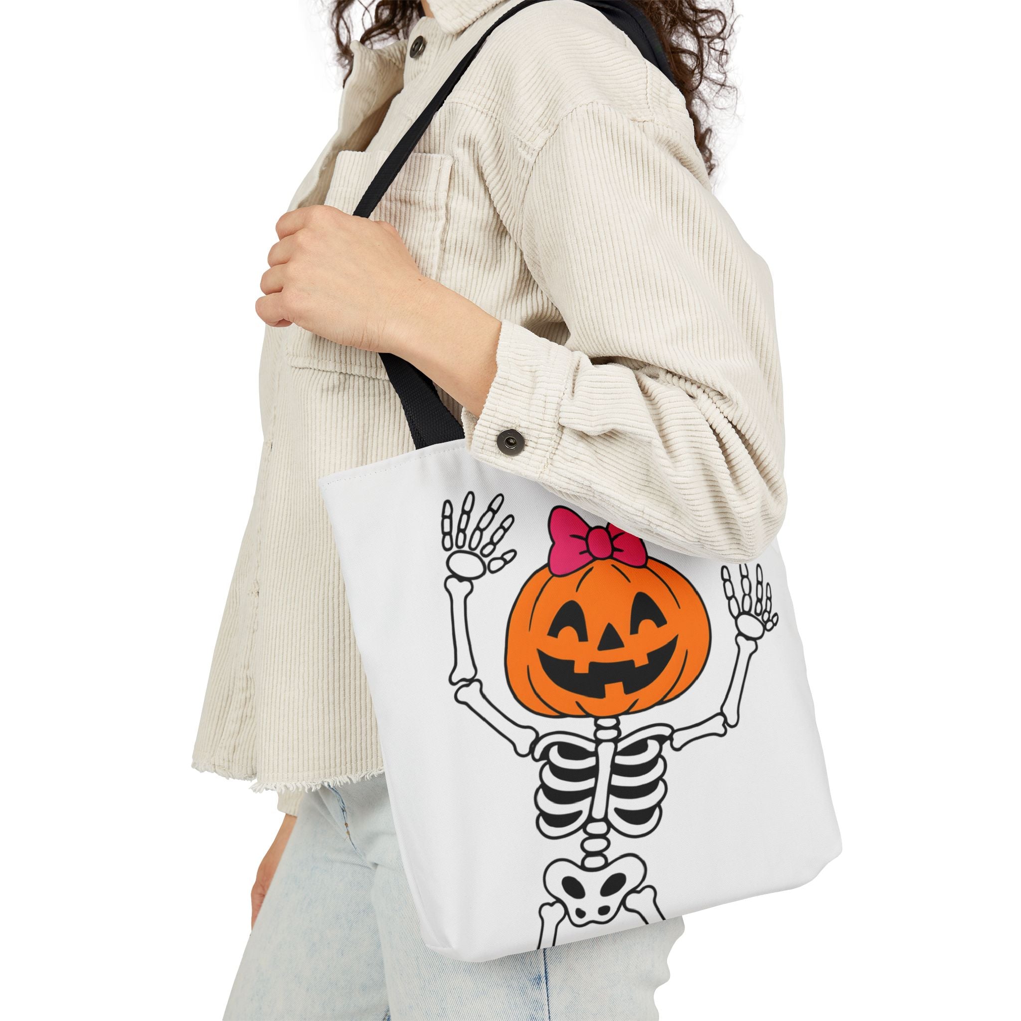 White canvas tote bag with black handles, cartoon pumpkin skeleton hands-up graphic