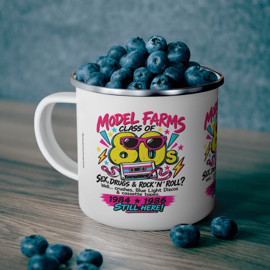 White enamel camping mug with colorful retro cassette graphic and wide handle, filled with blueberries