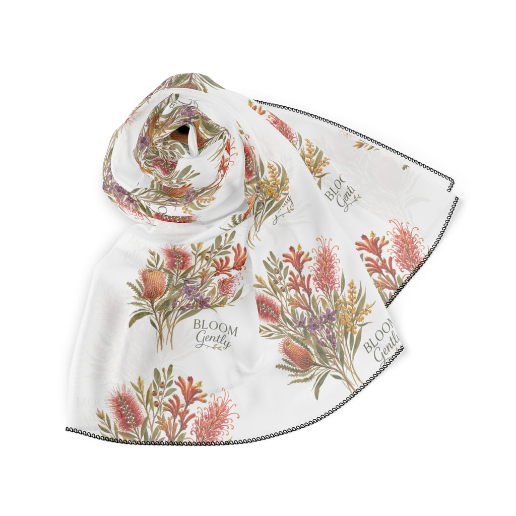 White poly scarf with coral floral bouquets and “Bloom Gently” text, draped with dark trim.