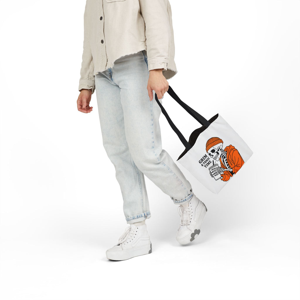 Canvas tote bag held to side, white with black handles; Grim & Tonic Time skeleton print